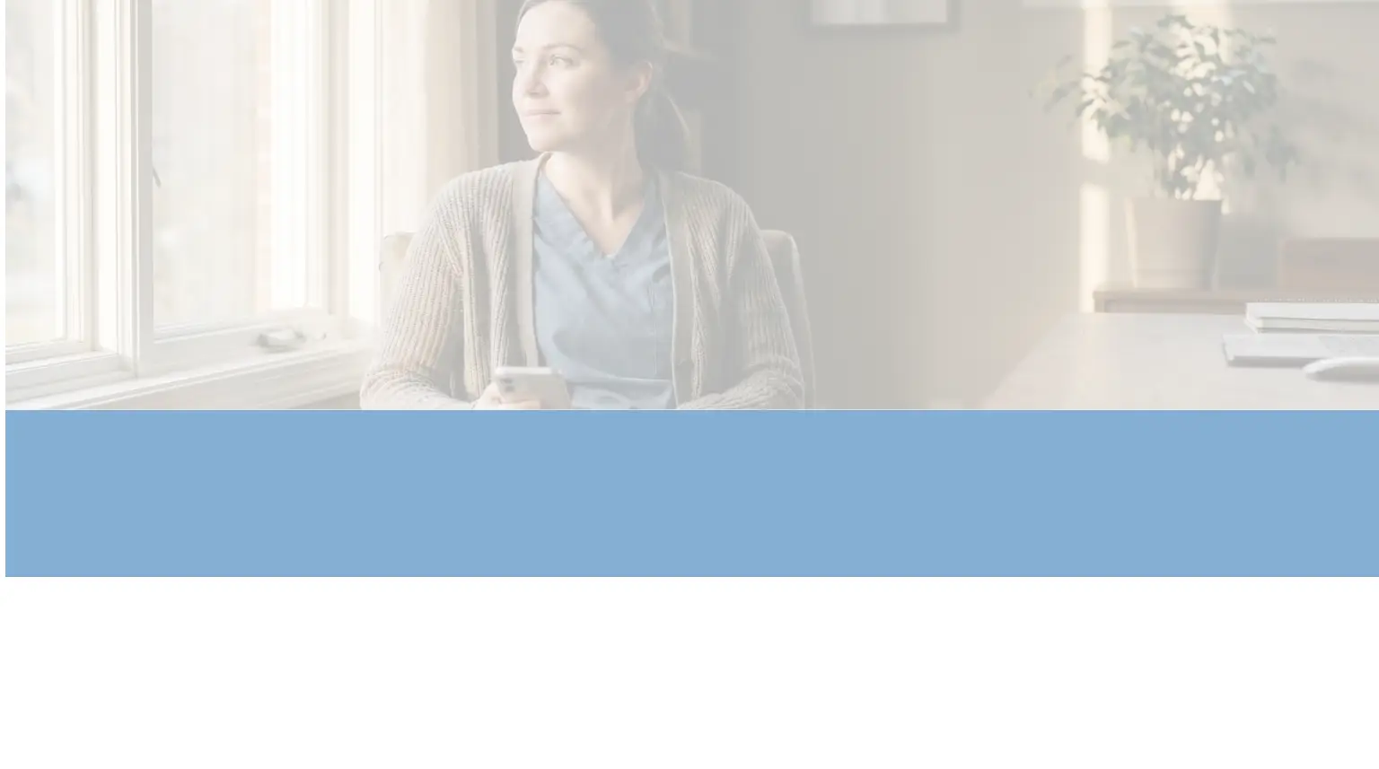 A woman dressed in blue nurse scrubs and a brown knitted cardigan sits in a leather armchair next to a large window in a home office. She holds a smartphone in her hands and gazes contemplatively out the window. Warm sunlight streams in from the left, illuminating her face and the cozy room, which contains a wooden desk, a potted plant, and a bookshelf.