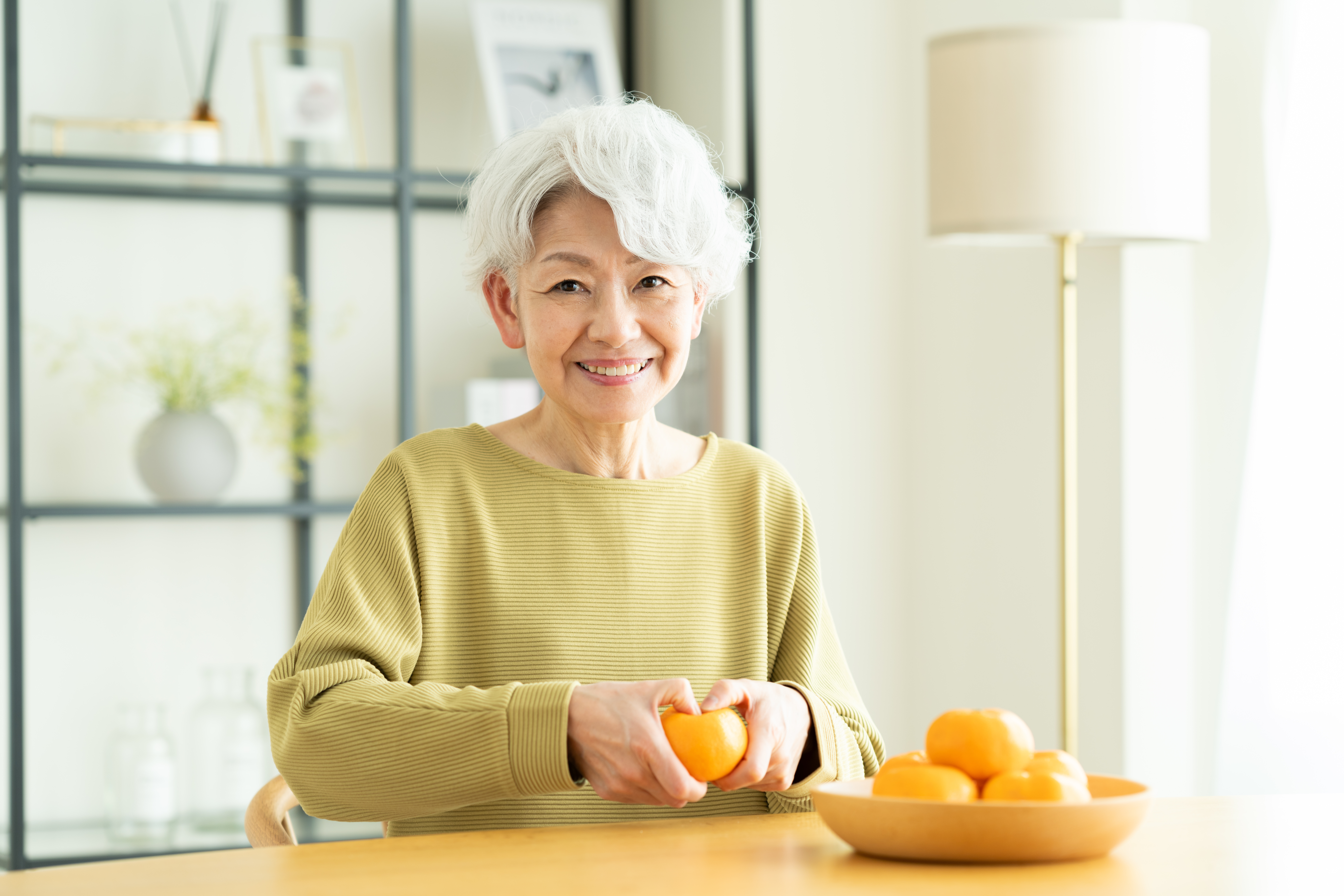 Senior woman peeling orange at kitchen counter with a smile