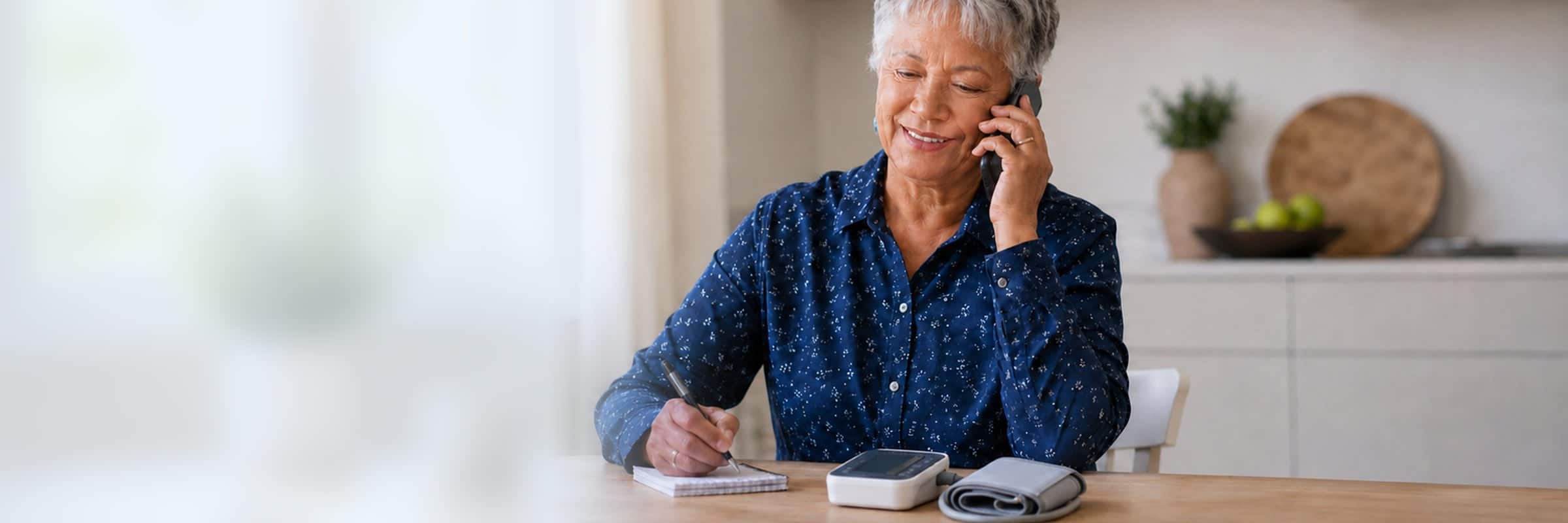 Older adult speaking with her care team by phone during CCM enrollment, home blood pressure monitor on the table.